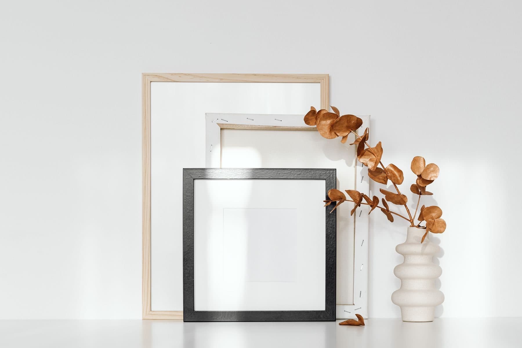 Empty picture frames and a vase of dried eucalyptus on a white table